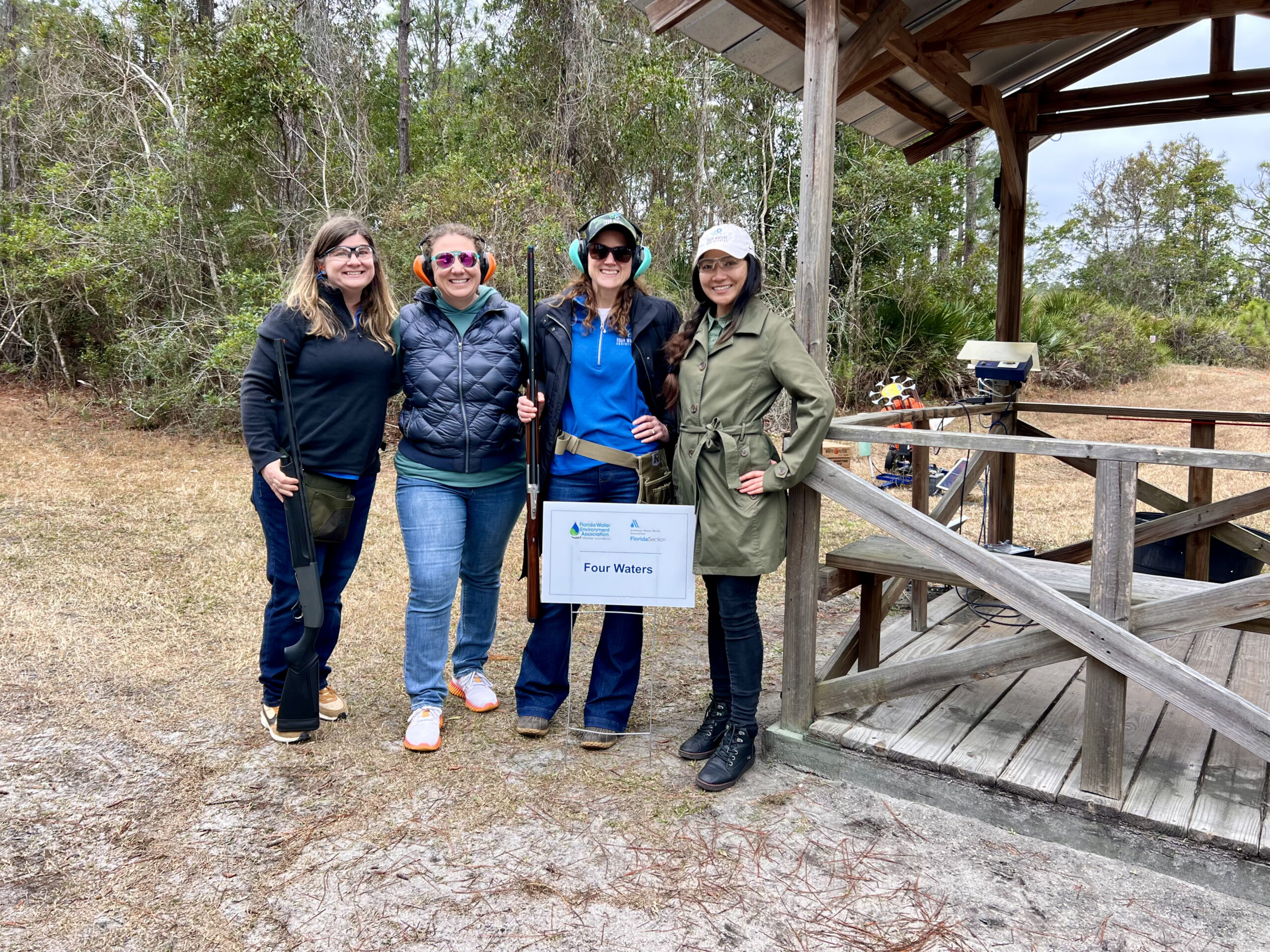 Four Women standing with guns by a sign that says Four Waters